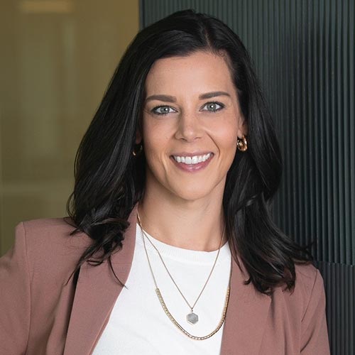Joanna Vosburg; A portrait of a dark brown haired woman wearing a white shirt and dark pink blazer, smiling at the camera.