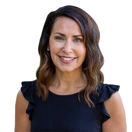 Niki Stotler; A woman with shoulder-length brown hair and a warm smile is wearing a black top with ruffled sleeves. The background is plain white, creating a professional tone.