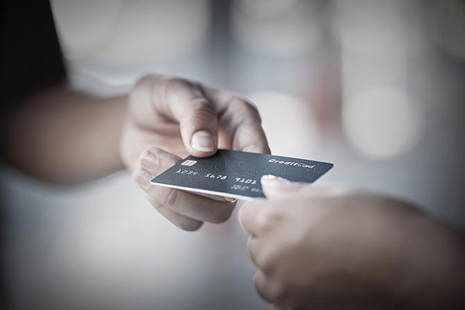 What Colorado’s Banking Community Needs to Know About Financial Abuse; Two hands are exchanging a black credit card in a blurred, neutral-toned setting. The image conveys a business or transaction moment.