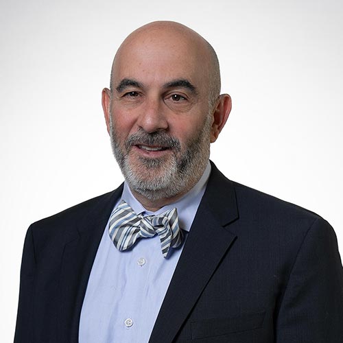 Lance Jacobs, A bald man with a beard in a dark suit and striped bow tie smiles gently at the camera. The background is plain white, conveying a professional tone.