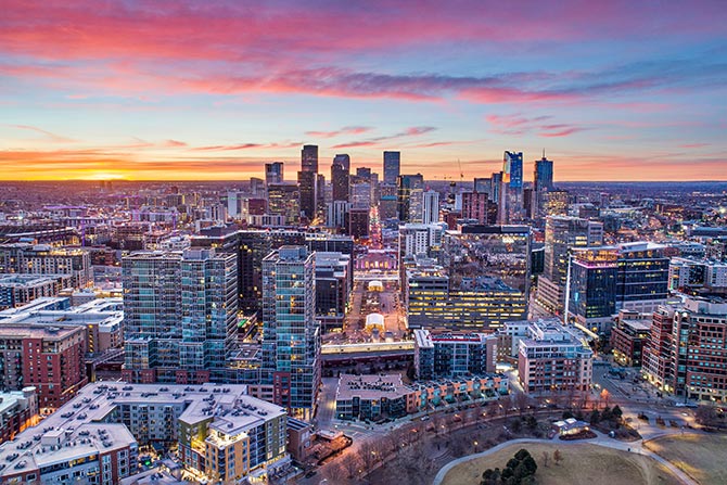 A View from the Capitol: Navigating a Critical Legislative Session for Colorado Banking; Aerial view of a city skyline at sunset. Tall buildings and skyscrapers are illuminated under a vibrant sky with pink and orange hues, conveying a peaceful urban scene.