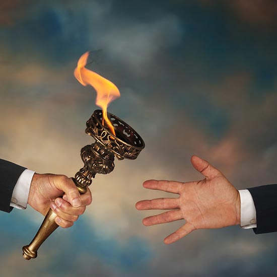 Arm and hand of a business man holding a metal flaming torch, passing it to another business person's hand