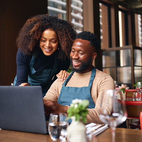 Utilizing-Risk‑Mitigating Feature. - Two business owners smiling and looking at a laptop screen together